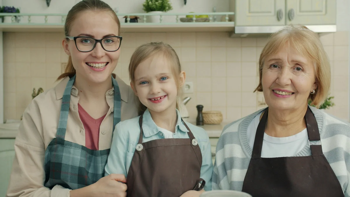 Portrait of happy family women and small girl in aprons smiling sitting in kitchen together looking at camera. Lifestyle, cookery and people concept. - family learning activities