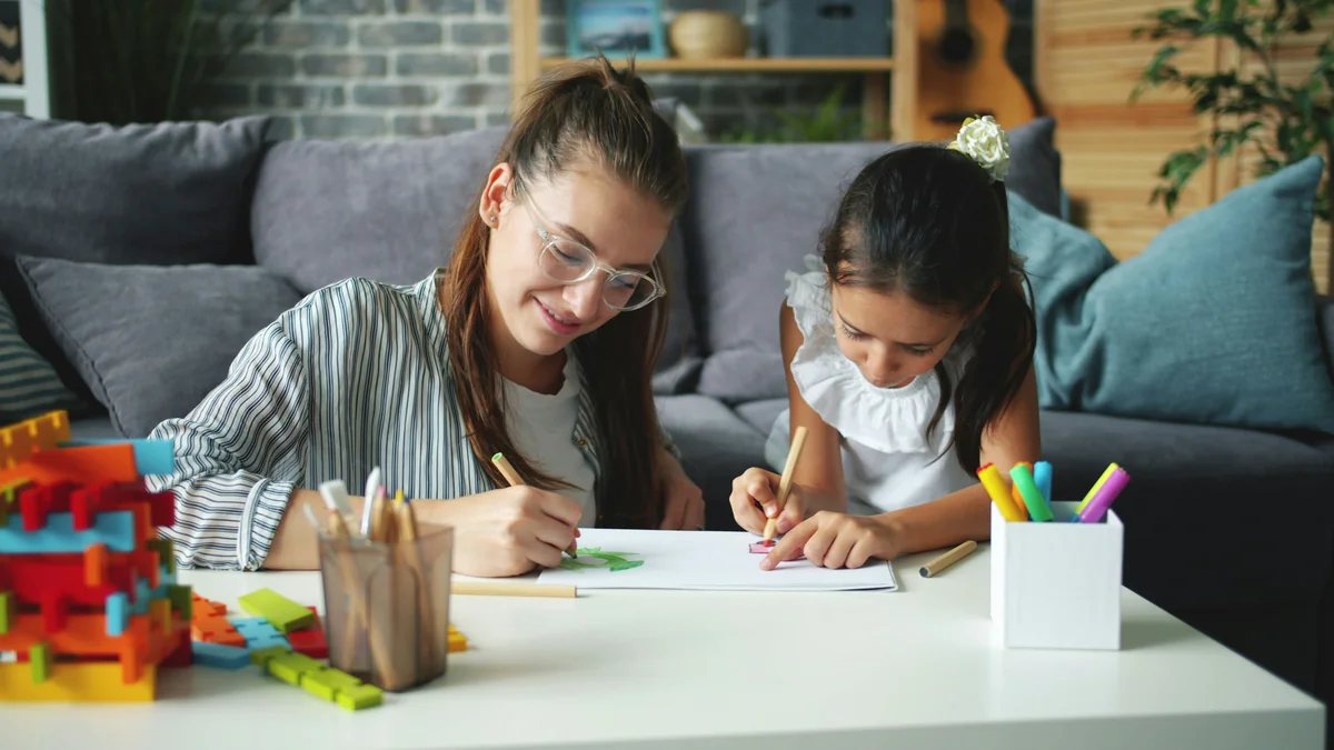 Cute little girl creative child is drawing picture while caring mother is helping expressing love. Leisure time at home, people and happy family concept. - home schooling strategies