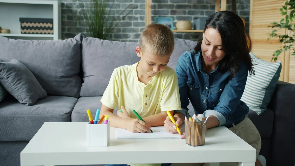 Small boy is drawing with markers together with caring mother in cozy room at home enjoying activity making picture. Creative kids and loving parents concept. - home schooling strategies
