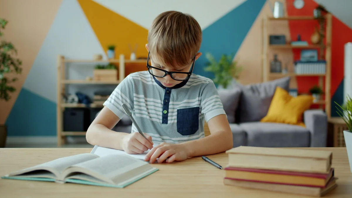 Portrait of cheerful child boy doing homework then looking at camera and smiling sitting at desk at home. Education, childhood and intellect concept. - home schooling strategies