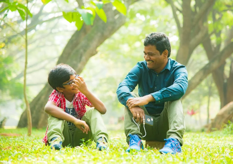 Happy father and son sitting on grass, sharing joyful moments outdoors. - parentchild communication